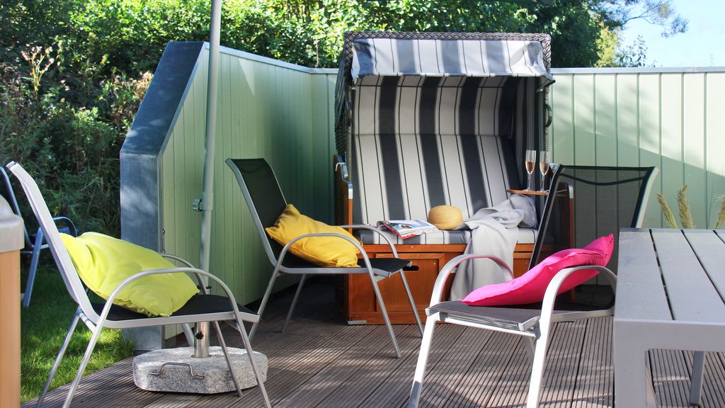 gepflasterte Terrasse mit Gartenstühlen, Tisch und Strandkorb, anderthalb Seiten sind von einer undurchsichtigen Wand umgeben