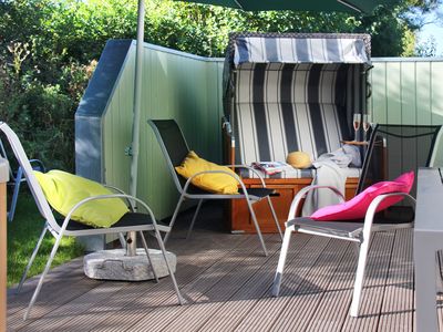 gepflasterte Terrasse mit Gartenstühlen, Tisch und Strandkorb, anderthalb Seiten sind von einer undurchsichtigen Wand umgeben